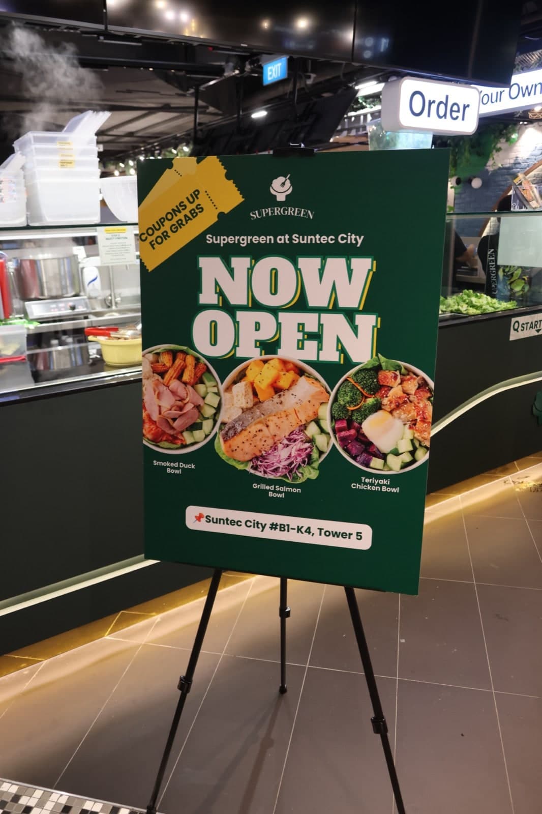 Now Open standee at Supergreen Suntec City, listing the Smoked Duck, Grilled Salmon, and Teriyaki Chicken bowls
